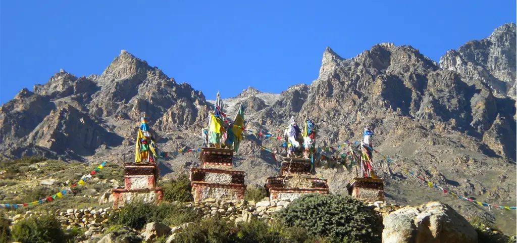 Colorful Buddhist prayer flags flutter above stone chortens in the remote Limi Valley of Humla, showcasing the cultural heritage found during monsoon treks in Nepal.