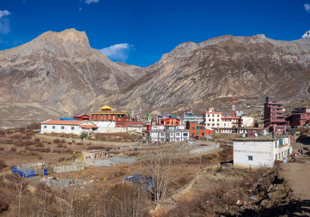 Panoramic landscape of a traditional mountain village with red-roofed buildings nestled beneath steep cliff faces in Upper Mustang.